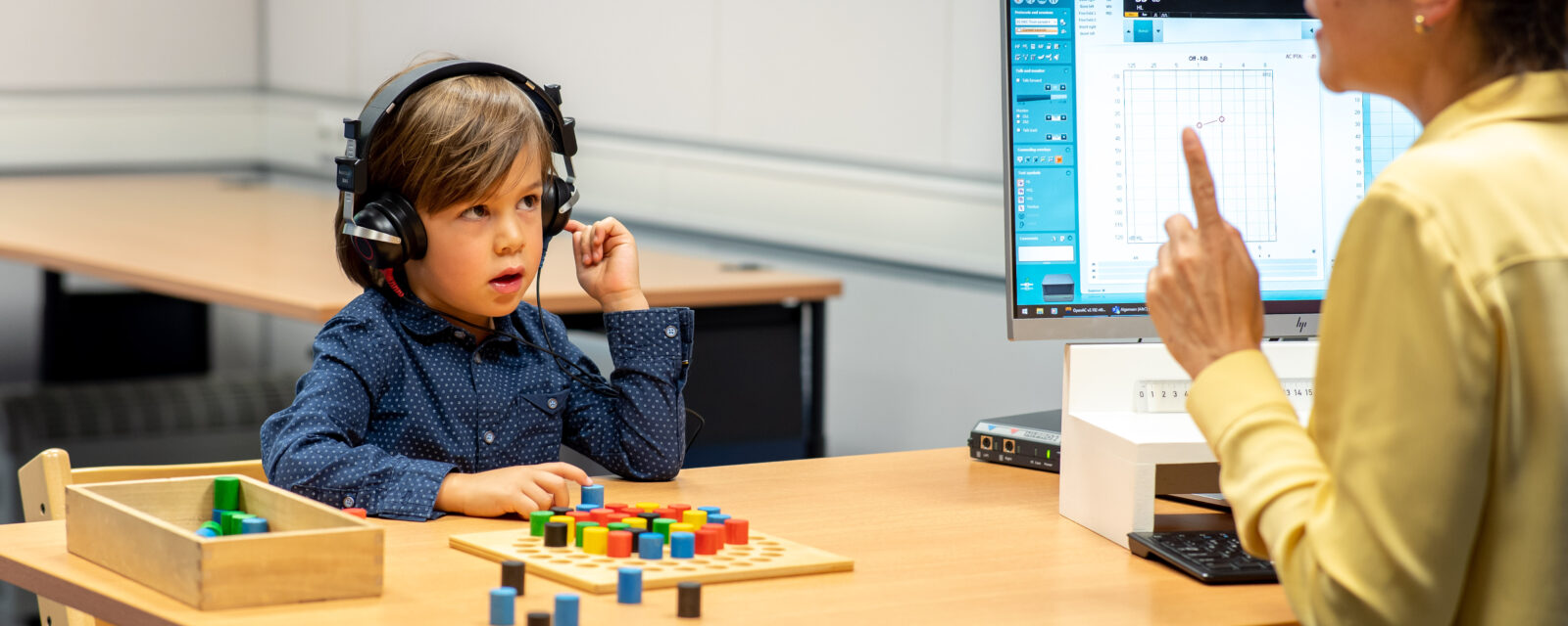 Een audiologieassistent neemt een gehoortest af bij een kind